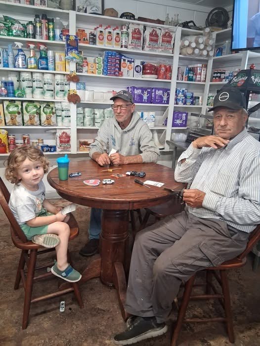Elijah, a small child, sits with two men at a table in the convenience store.