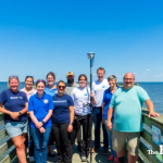 A group of people stand on a dock, posing with the new HydroNet water sensor